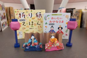 An origami set of Emperor, Empress and two lamps in front of two Japanese language learning books.